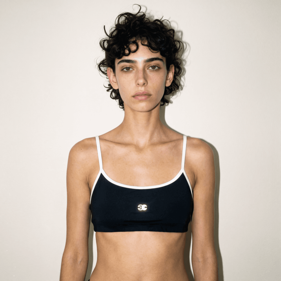 Model wearing the black Velocity Track Bra with white contrast piping, scoop neckline, slim straps, and Conscious Choice logo.